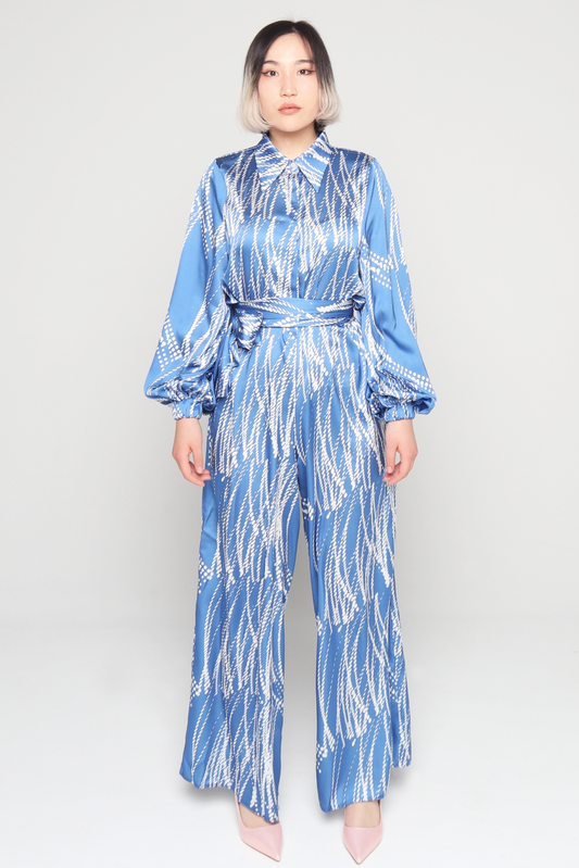 Woman wearing Blue and white collared hidden buttons side pockets elasticated balloon sleeves beautifully patterned satin Jumpsuit falls loosely through the legs with detachable belt A perfect Tznius style summer outfit for women